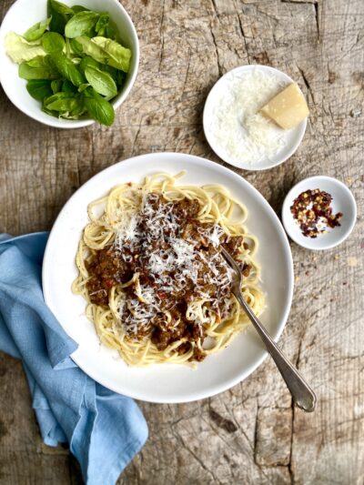 shallow bowl containing vegetable bolognese with spaghetti, parmesan and a salad
